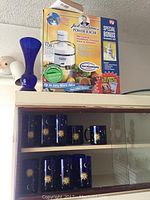 Juicer box and blue sun and moon decorated glasses and mug displayed on wood cabinet shelf.