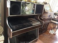Full view of woodgrain veneer console with chrome trim, integrated speakers, mirrored disco ball chamber and lower reflective panel