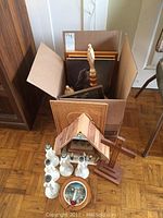 Photo showing open cardboard box with religious wood plaques and figurines outside box including wooden nativity stable, wooden cross and six white angel-shaped candle holders.