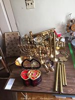 Photo of assorted brass candle holders including menorah, taper holders, brass rooster, heart-shaped music box, brass wind chimes rods, and assorted candles on wooden table.