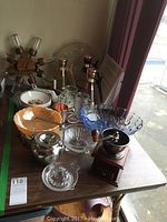 View of the kitchenware lot including wooden spice wheel, coffee grinder, glass bowls, mugs, jugs and metal teapot on a table.