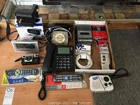 Overview photo showing all items including rotary phone, AT&T phone, Polaroid camera, remotes, clocks, and tapes laid out on carpet.