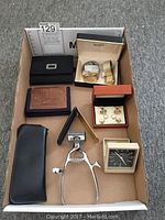 Overview photo showing all items in the lot including watches, wallets, cuff links, hair clippers, and a small clock.