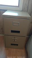 Front view of two-drawer beige metal file cabinet showing handles, label holders, and ventilation slots. Bottom drawer locked with key.