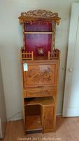 Front view of the carved wooden cabinet showing dragon-themed door and upper red panel with intricate top carving.