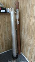 Two rolls standing upright against a wood panel wall. One roll wrapped in plastic, white color indicating the vapour barrier. The other roll with a wood grain vinyl flooring.