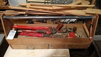 Wooden tool chest open showing pipe wrenches, wood lathe tools, monkey wrench, and a metal bar inside the lid