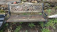 Front view of weathered wood and metal garden bench with lattice top backrest and slatted seat on grass.