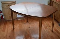 Full view of mid-century walnut extendable table with no leaves inserted, showing rectangular top with slight curve on edges and four tapered legs.