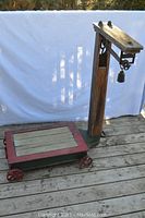 Full view of antique platform and scale beam showing wooden platform on metal frame with cast iron wheels and vertical beam with hanging weight