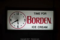 Front view of the rectangular lighted clock showing the clock face and Borden's Ice Cream advertising text illuminated brightly.