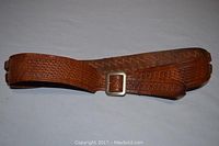 Detailed photo of the brown leather bandoleer showing textured leather and metal buckle, laid flat.
