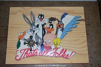 Wood plaque clock featuring multiple Looney Tunes characters including Bugs Bunny, Sylvester, Taz, Daffy Duck, Porky Pig, Tweety, and Road Runner with a clock mechanism and 'That's All Folks!' pink script.