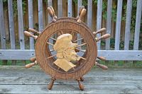 Front view of wooden ship's wheel showing captain's face carving in center and eight turned handles