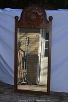 Full view of the tall rectangular wood framed mirror showing the entire mirror surface and top scalloped arch with sun carving and finials.