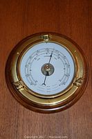 Front view of the brass rimmed wood mounted barometer showing the dial and pressure readings.