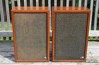 Pair of Pro Linear Stage 5 vintage speakers with walnut wood veneer cabinets and black textured fabric fronts, sitting outside on a wooden deck.