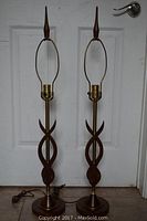 Pair of tall vintage lamps in twisted teak design with brass accents and cords, no shades attached.