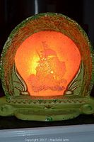 Close-up photo of the lamp lit from behind showing illuminated sailing ship silhouette and textured ceramic frame in green and brown.