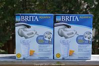 Two unopened Brita AquaView On Tap Faucet Water Filters shown side by side on outdoor surface with clear blue sky background