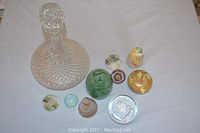Wide view showing all nine paperweights and the large textured glass decanter with stopper.