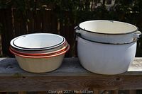 Two white enamelware pots with side handles and black rims showing chipping and age wear.