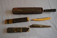 Photo of two straight razors, one with yellow handle and one with dark handle, alongside a wooden handled sharpening tool