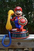 Front view showing Mario figure holding yellow handset and rotary dial with Nintendo branding.