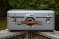 Front view of the silver-gray metal carrying box with brown leather handle and PHOTO SNIPER label.