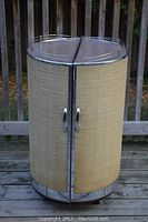Front view of closed barrel-shaped tiki bar showing tan ribbed vinyl exterior, chrome top and base, front doors.