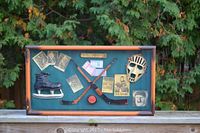Front view of shadow box with hockey memorabilia visible including crossed sticks, skate, goalie mask, puck, and photographs.