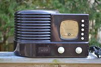 Front side view of the full radio unit showing the grille speaker on left, tuning dial, and control knobs on right.