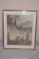 Full view of the framed black-and-white Native American print featuring multiple teepees, a chief in a feathered headdress, and group of seated warriors with a mountainous background.