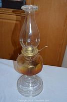 Full view of vintage glass hurricane oil lamp showing amber-colored fuel reservoir, clear chimney with beaded rim, and metal burner with wick roller.