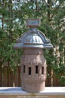 Full view of the vintage fence post topper showing rusted iron top with an ornate design and weathered wooden body with vertical cutouts.