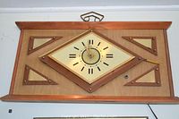Front view of vintage mid century modern wall clock showing wooden frame and diamond-shaped clock face with Roman numerals and geometric wooden design