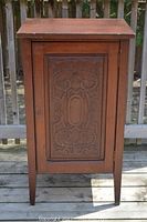 Front view of vintage wooden cabinet showing single door with intricate carved decorative pattern.