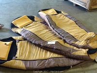 Photo showing three tan and brown Sleep Cell sleeping bags laid out on the floor, each with built-in sleeping pads visible by the bag shape and thickness.