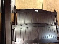 Wooden king size bed headboard and one side rail leaning against wall with visible vertical slats and turned finials on posts.