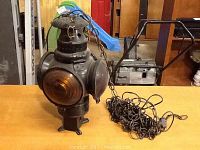 Photo of a vintage hanging lamp with chain and power cord extending from top, showing amber lens on front and metal body with ventilation holes.