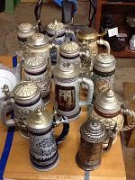Twelve assorted beer steins displayed on a table, showing pewter lids and relief decoration.