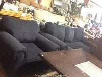 Navy blue fabric sofa and matching armchair set in a warehouse space, surrounded by other furniture and items.