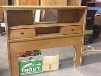 Queen size wooden headboard with two open shelves on top and two drawers below, showing front view in a storage or garage setting.