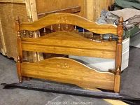 Wooden queen bed frame headboard and footboard with turned posts and carved detail, side rails laid below.