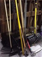 Photo showing a collection of yard tools including rakes, an edger, and a snow shovel leaning against a wooden pallet.