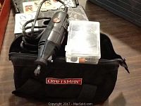 Black Craftsman rotary tool with power cord, plastic accessory case, and Craftsman carrying bag, all placed on a flat surface.