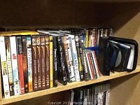 Shelf with assorted DVDs and CDs showing titles such as Flywheel, The Bodyguard, The Chronicles of Riddick, and others, along with a CD binder sleeve.