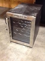 Vinotemp electric wine cellar cooler photographed from front-left angle showing exterior stainless steel frame, glass door with logo, and metal bottle racks inside.