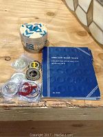 Photo showing a Lincoln Head Cent collection book, a small woven basket, and six coins mostly in plastic cases including military challenge coins and commemoratives.