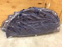 Navy blue folding chair inside a clear, plastic carrying bag with handles, placed on concrete floor against a wooden background.